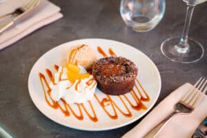 Fondant au chocolat servi avec glace, chantilly, quartier d'orange et filet de caramel sur assiette blanche.