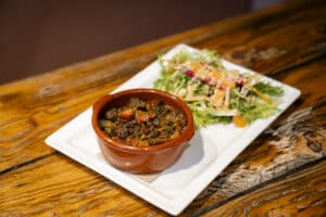 Plat de migas croustillantes dans un ramequin en terre cuite servi avec une salade verte et une sauce crémeuse sur une table en bois rustique.