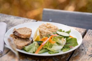 Rillette de poisson avec pain complet, salade fraîche et quartier de citron sur table en bois extérieur.