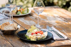 Salade de pommes de terre et œufs de caille sur table en bois rustique avec pain et verres à l'extérieur.