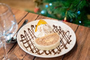 Bûche glacée au chocolat et crème, garnie de chantilly, d'une tranche d'orange et décorée de chocolat, sur fond de sapin de Noël.