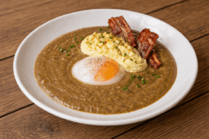 Œuf poché au poivre noir et purée onctueuse, accompagnés de bacon croustillant, servis dans une riche sauce brune de type gravy.
