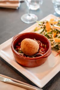Arancini croustillant sur chili dans un bol en terre cuite avec salade composée fraîche et croquante.