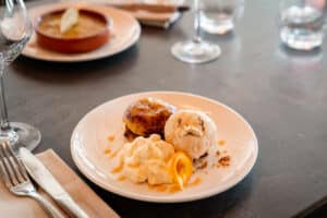 Assiette de dessert avec pâtisserie caramélisée, glace vanille, crème fouettée et zeste d'orange dans un restaurant.