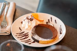 Tartelette au chocolat fondante, crème fouettée et quartier d'orange sur une assiette blanche décorée de coulis.