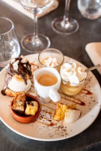 Café gourmand avec profiterole au chocolat, espresso et mignardises sucrées sur une assiette décorée.