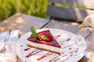 Cheesecake aux fraises frais avec coulis de fruits rouges et menthe servi en terrasse ensoleillée.