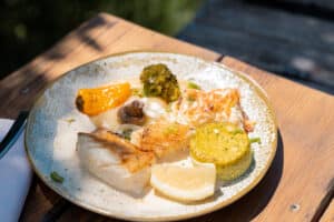 Poisson blanc poêlé, brocoli, poivron et sauce crémeuse servis sur une table en bois au soleil.