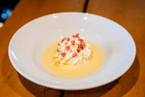 Île flottante avec crème anglaise, caramel et brisures rouges dans une assiette blanche sur bois.