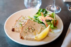 Terrine de poisson au homard avec salade fraîche et quartier de citron sur une assiette blanche élégante.