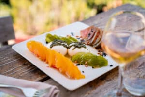 Salade de tomates anciennes, burrata au pesto et pignons de pin servie en terrasse avec un verre de vin.