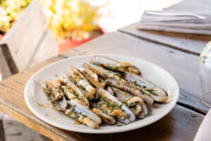 Couteaux de mer grillés à la persillade et ail, servis sur une table en bois en terrasse.