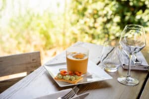 Gazpacho frais, toast au pesto et tomates cerises sur table en bois en terrasse ensoleillée.