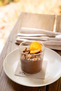 Mousse au chocolat noir, noisettes concassées et orange confite dans un verre sur table en bois.