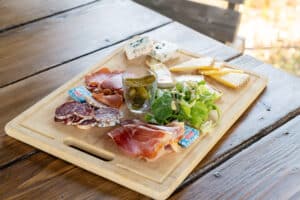 Planche de charcuterie et fromages avec jambon cru, saucisson, brie, bleu, pickles et beurre Paysan Breton sur bois.