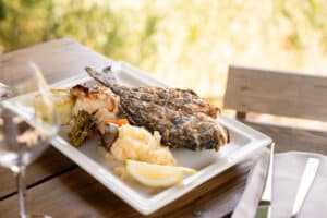 Poisson grillé entier, purée et légumes frais servis sur une table en bois en terrasse.