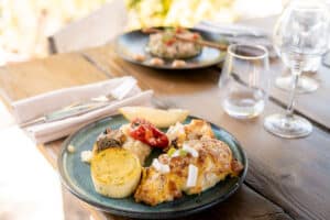 Poisson grillé au fromage, flan aux herbes et poivron rôti servis sur une table en bois ensoleillée.