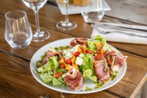 Salade fraîche au jambon cru, melon, feta et tomates cerises sur une table en bois rustique.