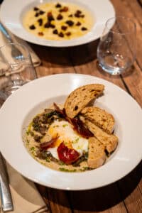 Œuf poché, champignons et jambon croustillant avec toasts de pain grillé servis dans une assiette blanche.