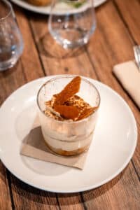 Tiramisu onctueux en verrine décoré de tuiles au caramel croquantes, servi sur une table en bois rustique.