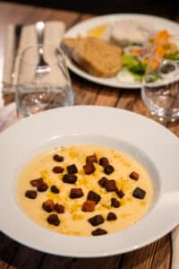 Velouté de légumes onctueux garni de croûtons grillés et petits dés, servi sur une table en bois de restaurant.